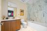 Bathroom featuring a wood-finish vanity with a light-toned countertop, a frameless glass shower enclosure, large-format tile shower surround, and tile