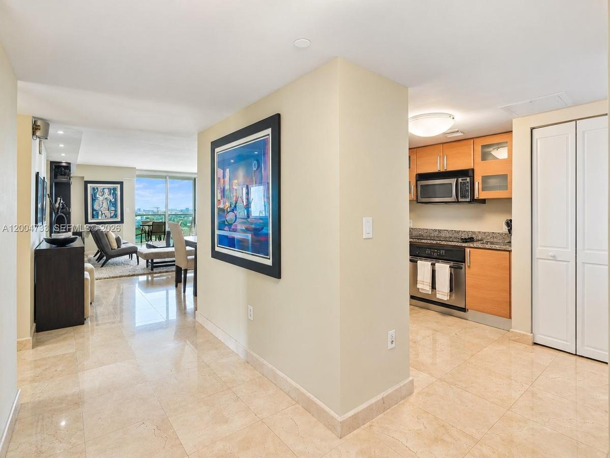 Polished stone flooring throughout, kitchen featuring wood-finish cabinetry, stone countertops, stainless steel appliances, and built-in closet storag