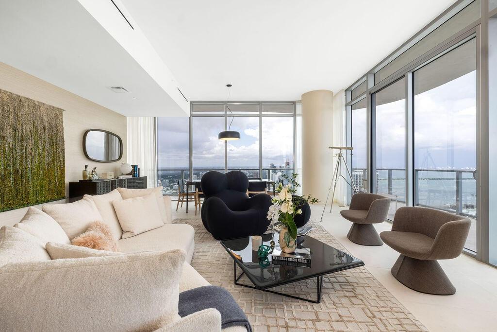 Floor-to-ceiling glass walls, sleek cylindrical architectural column, recessed linear lighting, polished neutral flooring, and integrated balcony acce