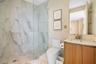 Walk-in shower with floor-to-ceiling stone-finish wall tiles and a glass enclosure, wood-finish vanity with an integrated countertop sink, and a large