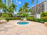 In-ground spa with stone tile surround, paver patio, metal handrail, perimeter hedges, and mature palms