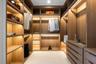 Custom closet featuring light wood-finish cabinetry, integrated LED shelf lighting, tiered hanging rods, and built-in dresser drawers with matte hardw