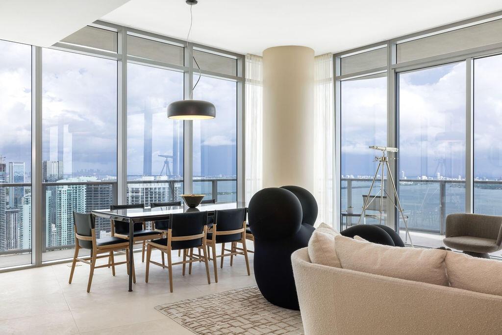 Floor-to-ceiling glass walls, wrap-around balcony with glass railing, large-format tile flooring, cylindrical structural column, and modern matte blac