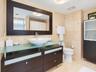 Bathroom featuring a vanity with a frosted glass countertop, vessel sink, dark wood-finish cabinetry, a large framed mirror, and natural stone tile fl