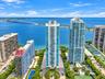 High-rise tower featuring glass-paneled balconies, floor-to-ceiling windows, and a waterfront location with immediate access to exterior tennis courts