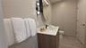 Modern vanity with wood-finish cabinetry, white countertop, integrated rectangular sink, matte black faucet, and oval mirror with wall-mounted lightin
