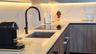 Kitchen featuring light-toned countertops, integrated under-cabinet lighting, wood-finish cabinetry, a square undermount sink, and a matte black high-