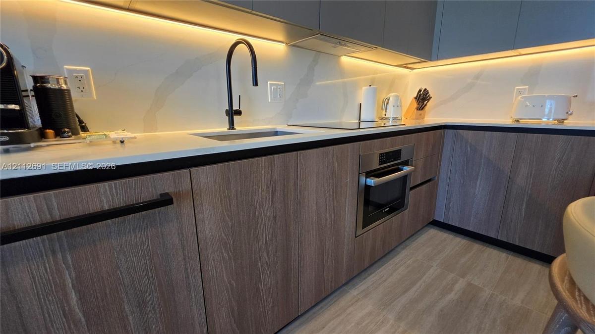 Kitchen featuring flat-panel wood-grain cabinetry, quartz countertops, integrated under-cabinet lighting, a matte black gooseneck faucet, and a stainl