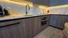 Kitchen featuring flat-panel wood-grain cabinetry, quartz countertops, integrated under-cabinet lighting, a matte black gooseneck faucet, and a stainl