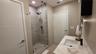 Bathroom featuring a walk-in shower with frameless glass enclosure, horizontal stone-finish tile surround, recessed lighting, white vanity with stone-