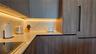 Kitchen featuring wood-finish cabinetry, solid surface countertops, a full-height backsplash, under-cabinet lighting, and integrated panel-ready appli