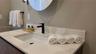 Vanity featuring a white countertop with integrated backsplash, undermount rectangular sink, matte black faucet, and circular wall-mounted mirror