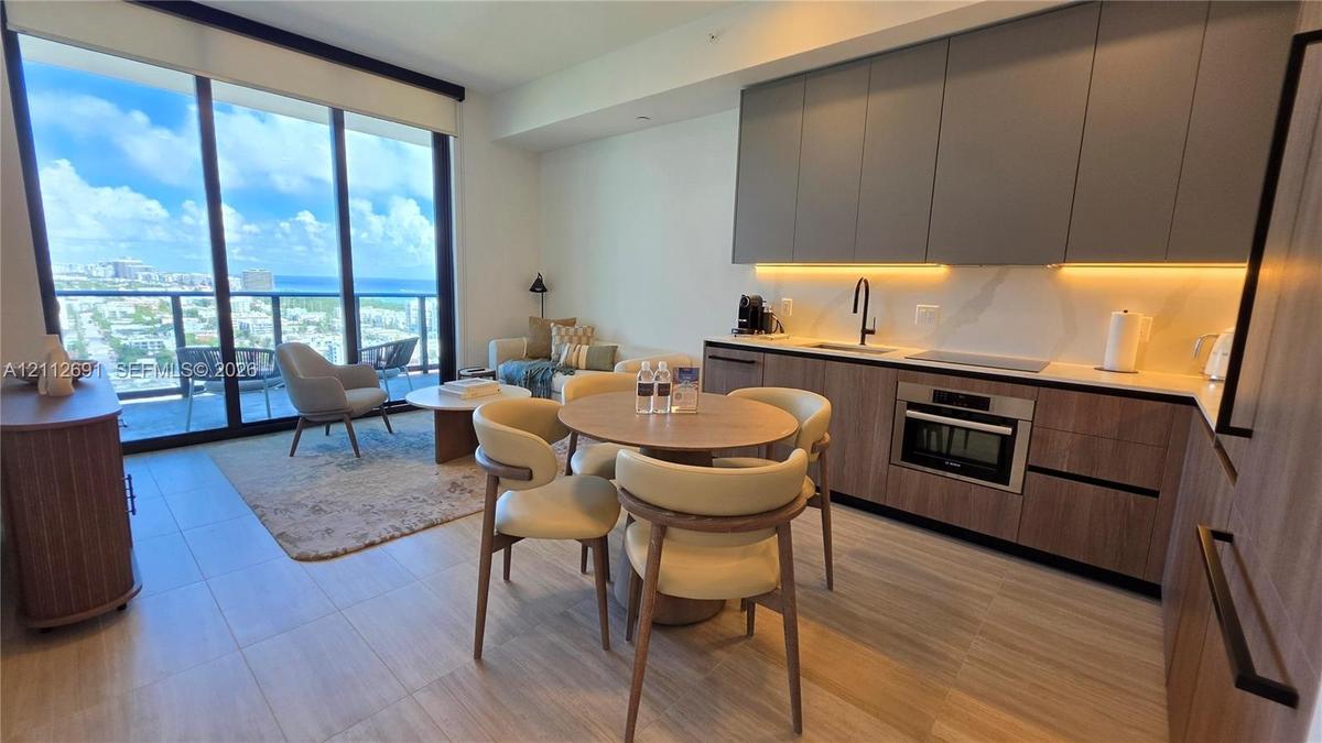 Modern kitchen featuring flat-panel wood-finish cabinetry, solid-surface countertops, integrated under-cabinet lighting, and floor-to-ceiling glass sl