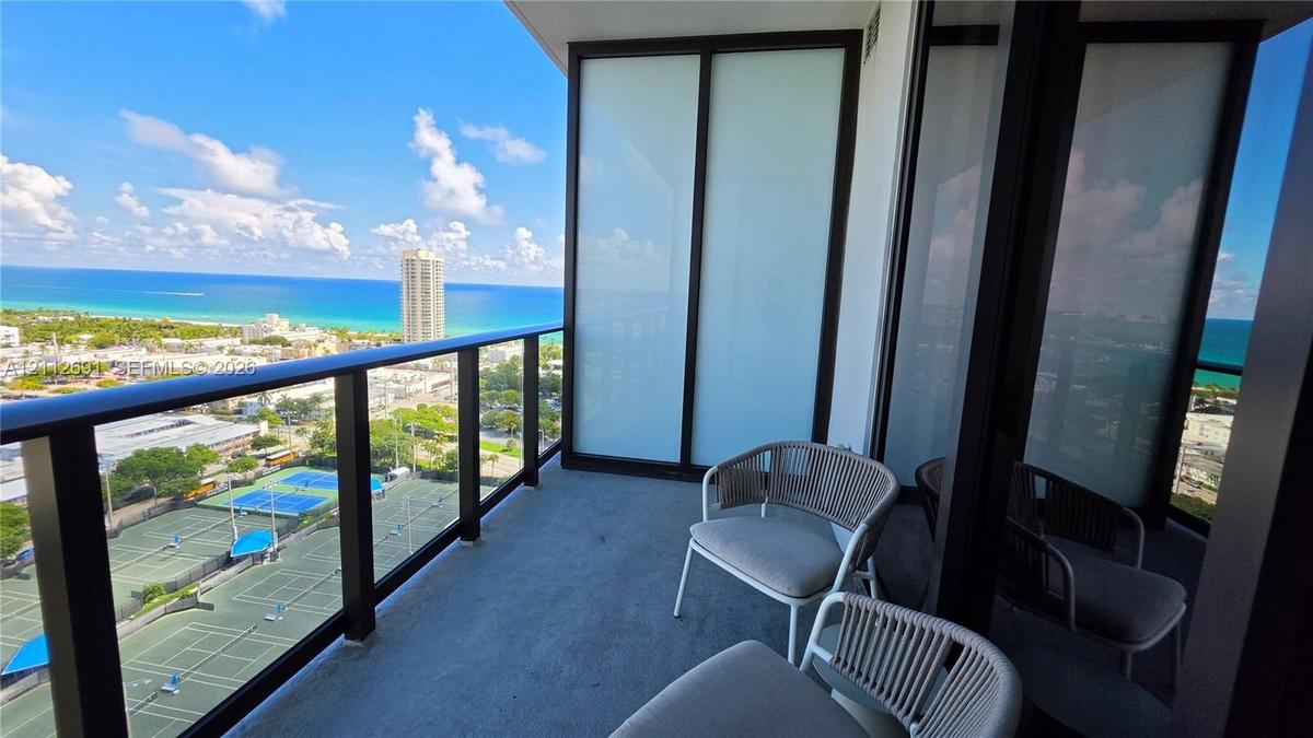 Private balcony featuring floor-to-ceiling glass paneling and black metal railing, overlooking coastal surroundings