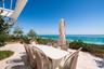 Expansive stone-paved terrace featuring a white pergola, transparent glass railing, and mature coastal landscaping