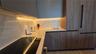 Modern kitchen featuring flat-panel cabinetry with wood-finish grain, integrated paneled refrigerator, solid-surface backsplash, under-cabinet lightin