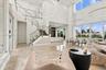 Double-height ceiling, floor-to-ceiling windows, polished tile flooring, glass-panel staircase railing, and modern circular pendant lighting