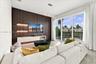 Living area featuring an accent wall with vertical fluted paneling, integrated floating cabinetry, custom illuminated shelving, a sculptural light fix