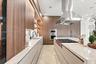 Kitchen featuring full-height wood-finish cabinetry, waterfall-edge stone countertops, stainless steel professional-grade range hood, built-in wall ov
