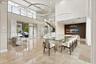 Double-height ceiling with large-scale circular pendant lighting, polished stone-finish flooring, glass-railed staircase, and decorative vertical wood