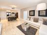 Open-concept interior featuring light-toned stone tile flooring, cabinetry with contrasting white and dark wood-finish surfaces, stainless steel kitch