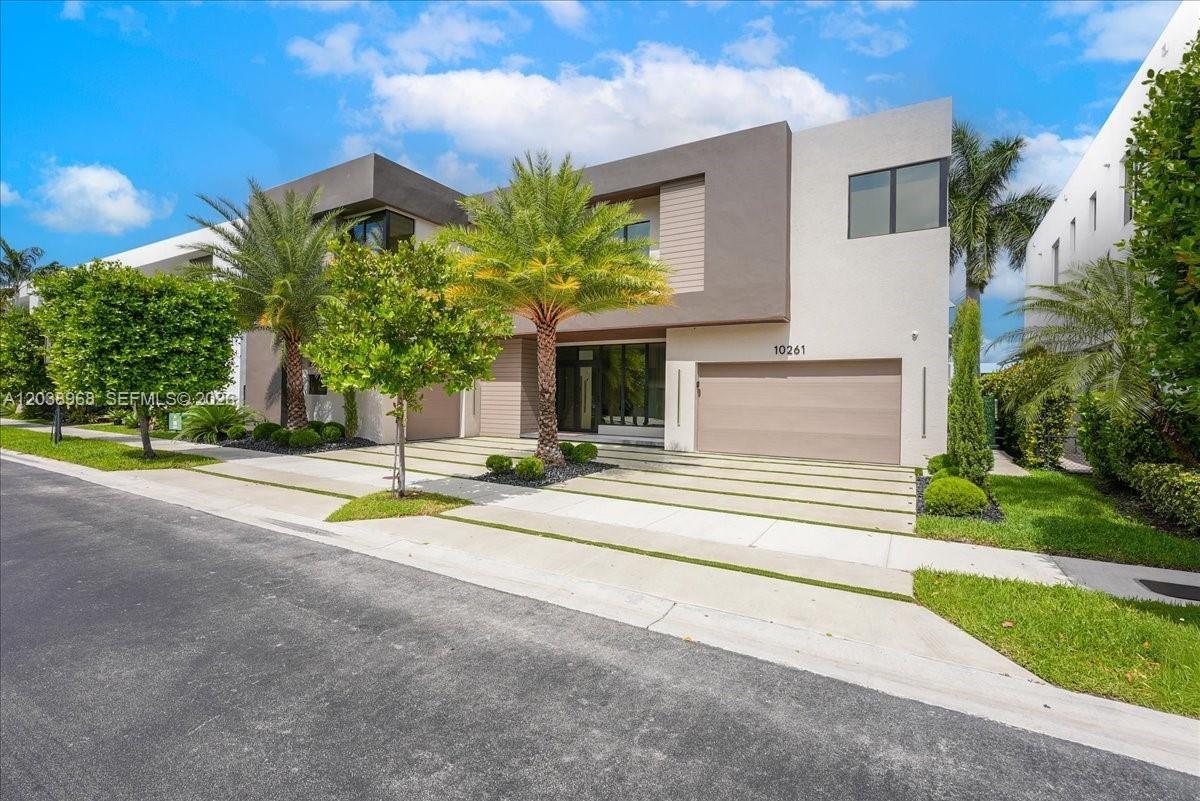 Modern two-story architectural exterior featuring a stucco facade, multi-tonal earth-tone finish, integrated multi-car garage, and concrete paver driv