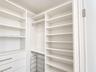 Custom white built-in storage system featuring floor-to-ceiling shelving, hanging rods, integrated drawers with horizontal pulls, and a metal wire rac