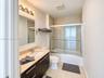 Modern vanity with integrated countertop and sink, wall-mounted light fixture, tile-surround shower with sliding glass doors, and light-tone floor til