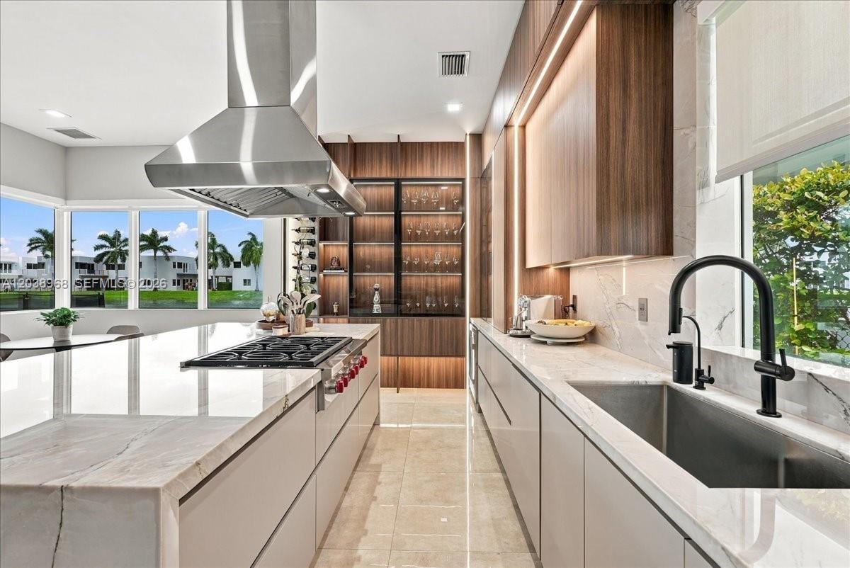 Contemporary kitchen featuring a stone-topped waterfall island, custom wood-finish cabinetry, stainless steel range hood, integrated display shelving 