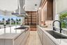 Contemporary kitchen featuring a stone-topped waterfall island, custom wood-finish cabinetry, stainless steel range hood, integrated display shelving 