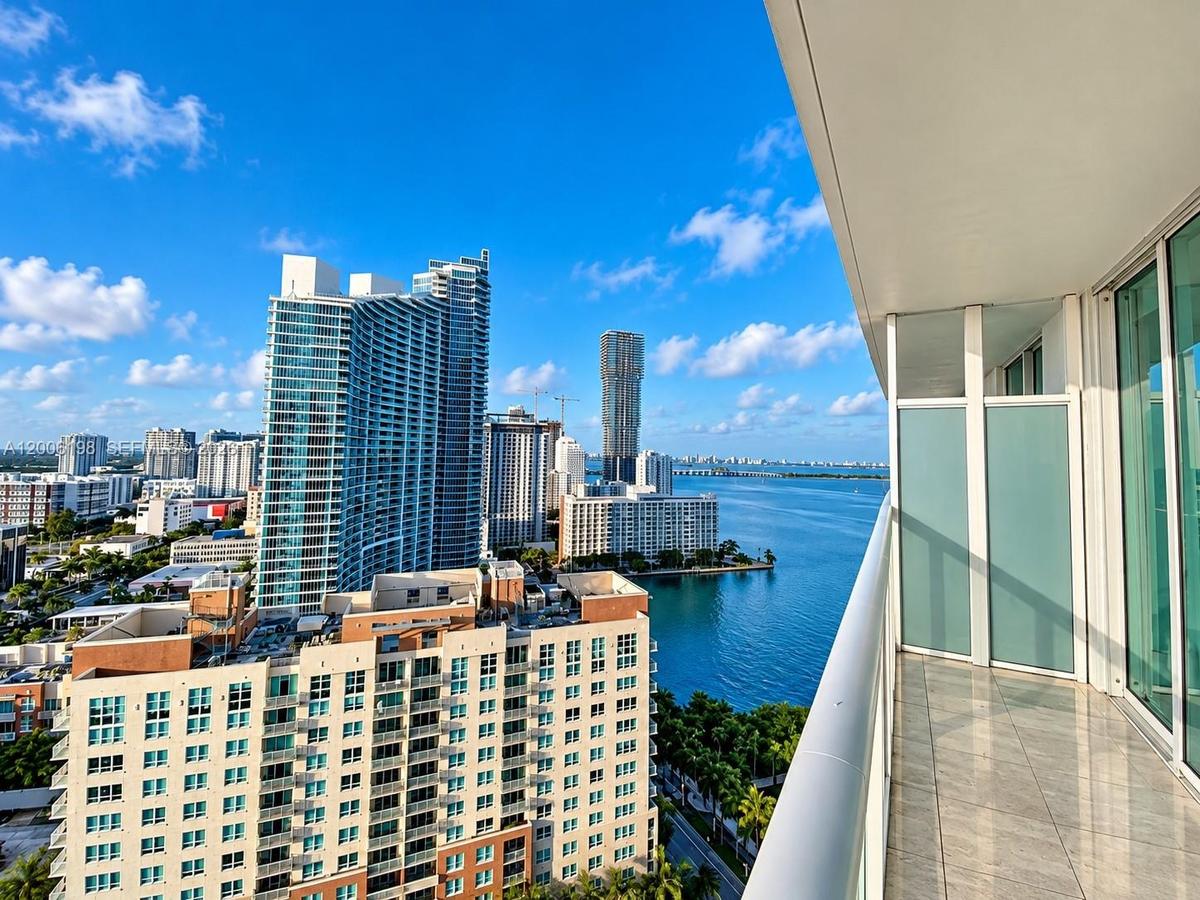 Private balcony with tile flooring, frosted glass privacy panels, and an aluminum railing, showcasing a water and skyline panorama