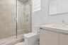 Glass-enclosed shower with large-format wall tile, light wood-finish vanity, light-toned countertop with integrated sink, and polished chrome fixtures