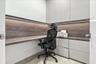 Built-in L-shaped wood-finish desk with integrated under-cabinet LED lighting, matte grey cabinetry, floor-to-ceiling storage, and solid-surface count