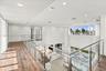 Open-concept landing featuring wood-finish flooring, glass-panel railing with metal hardware, recessed lighting, and double-height windows