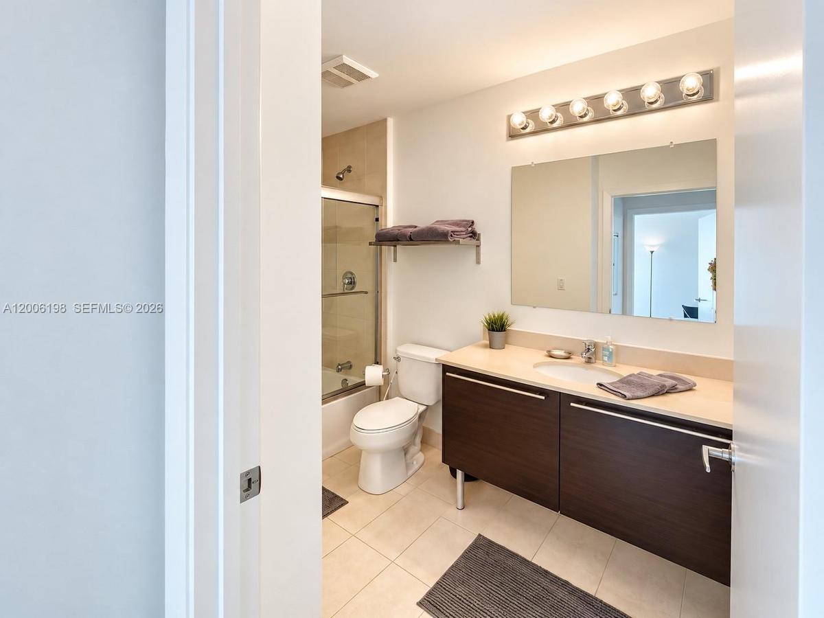 Bathroom featuring a floating vanity with dark wood-finish cabinetry, a solid-surface countertop with integrated sink, a large frameless mirror, and a