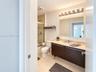 Bathroom featuring a floating vanity with dark wood-finish cabinetry, a solid-surface countertop with integrated sink, a large frameless mirror, and a