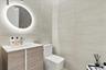 Modern vanity with a wood-finish cabinet and integrated sink, illuminated oval wall mirror, and large-format tile wall cladding