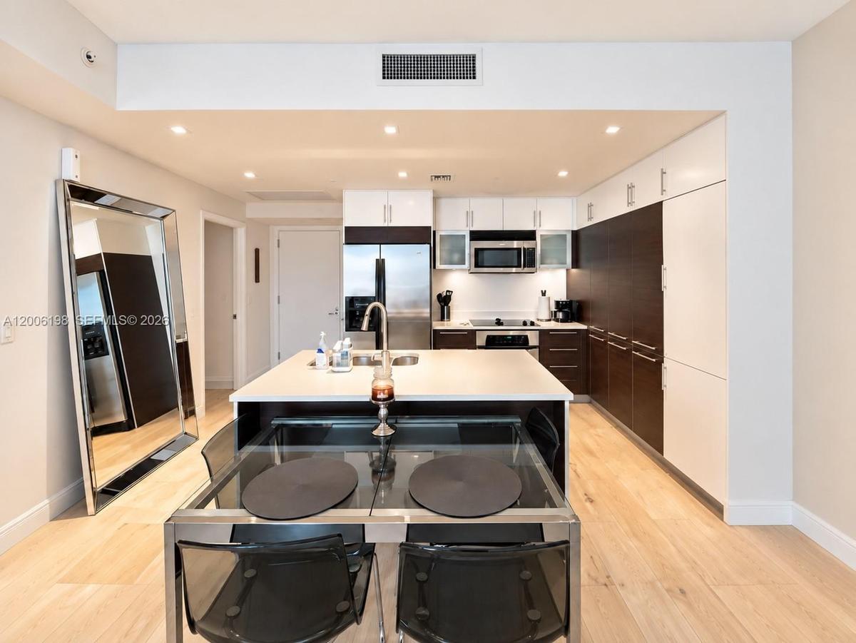 Modern kitchen featuring two-tone flat-panel cabinetry, a central island with a solid-surface countertop, stainless steel appliances, and wood-finish 