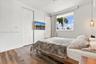 Wood-finish flooring, white walls, closet with bi-fold doors, horizontal window with palm tree exterior, and a single glass-shade pendant light
