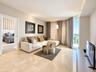 Living area featuring light-toned stone tile flooring, floor-to-ceiling windows, and a glass-paneled balcony