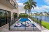 In-ground pool featuring stone paver decking, black mesh safety fencing, sliding glass doors, and waterfront positioning