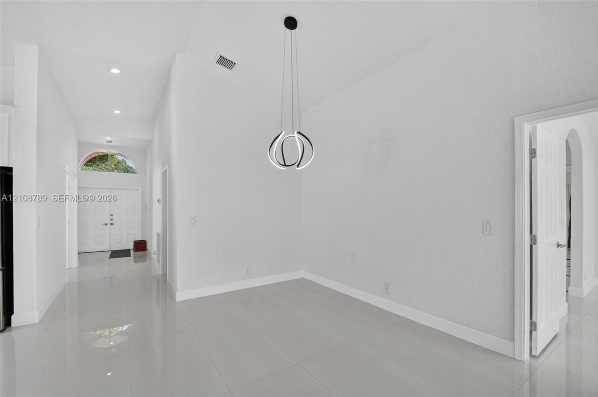 Vaulted ceilings, polished tile flooring, contemporary geometric pendant lighting, recessed ceiling lights, and double entry doors with an arched tran