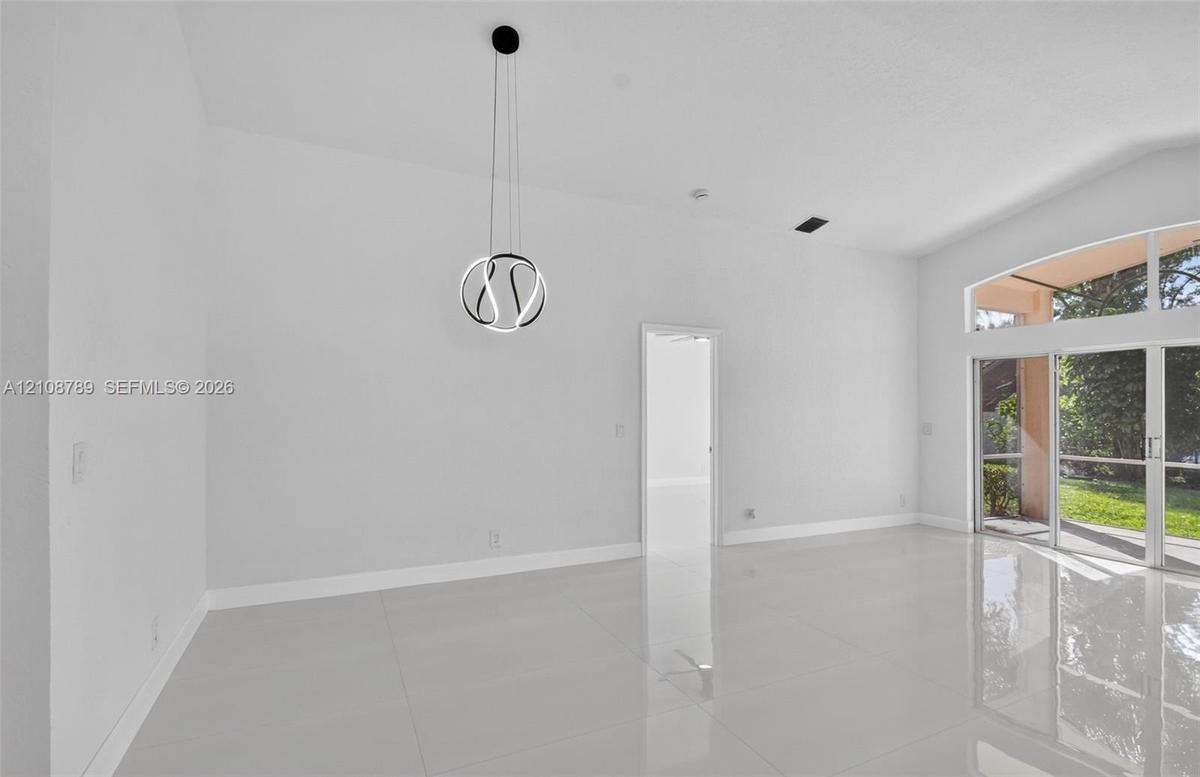 High-ceiling interior featuring polished tile flooring, a geometric LED pendant light fixture, and large glass sliding doors with transoms