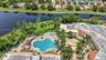 Aerial perspective of a sprawling complex featuring a large swimming pool, expansive paver patio, lush landscaping with mature palm trees, and direct 