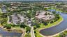 Aerial perspective featuring a multi-building property with an expansive paved parking area, water frontage, perimeter landscaping, and a central outd