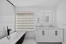Freestanding black and white soaking tub with matte black faucet, glass block window, double vanity with geometric cabinetry detail, and wall-mounted 