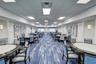 Expansive common area featuring a suspended drop ceiling, integrated recessed lighting, wall-mounted sconces, and patterned carpeted flooring