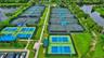 Recreational facility featuring multiple tennis courts, pickleball courts, paved walkways, and water frontage