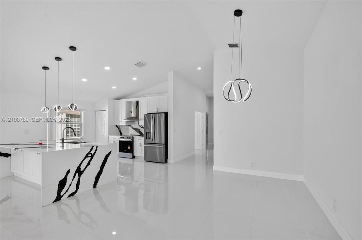 Open-concept kitchen featuring an island with high-contrast stone surfaces, white shaker-style cabinetry, stainless steel appliances, polished tile fl