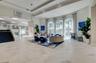 Expansive open-concept interior featuring recessed tray ceilings, large arched windows, stone-finish tile flooring, and a glass-paneled staircase with